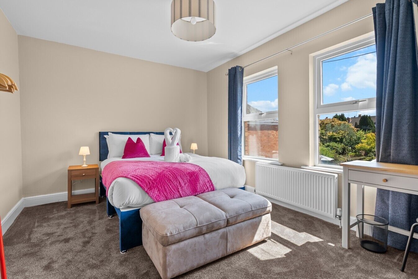 Une chambre à coucher comprenant un lit, des tables de chevet, un bureau, un radiateur et une fenêtre avec des rideaux.
