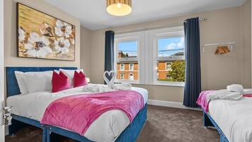 Une chambre d’hôtel avec deux lits, une grande fenêtre avec des rideaux, un tableau au mur et un luminaire au plafond.