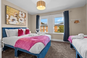 Een hotelkamer met twee bedden, een groot raam met gordijnen, een schilderij aan de muur en een plafondlamp.
