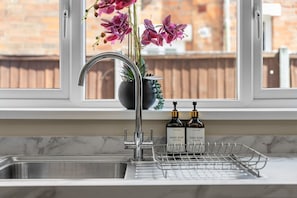 A kitchen sink with a modern faucet, a potted plant with purple flowers, and two bottles of hand and dish soap on the counter. - Luxury Home, Sleeps 12, Pool Table, Free Parking (Worcestershire)