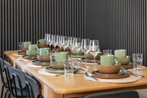 Een eettafel gedekt met groene keramische kopjes, kommen en wijnglazen, met een zwarte stoel links.