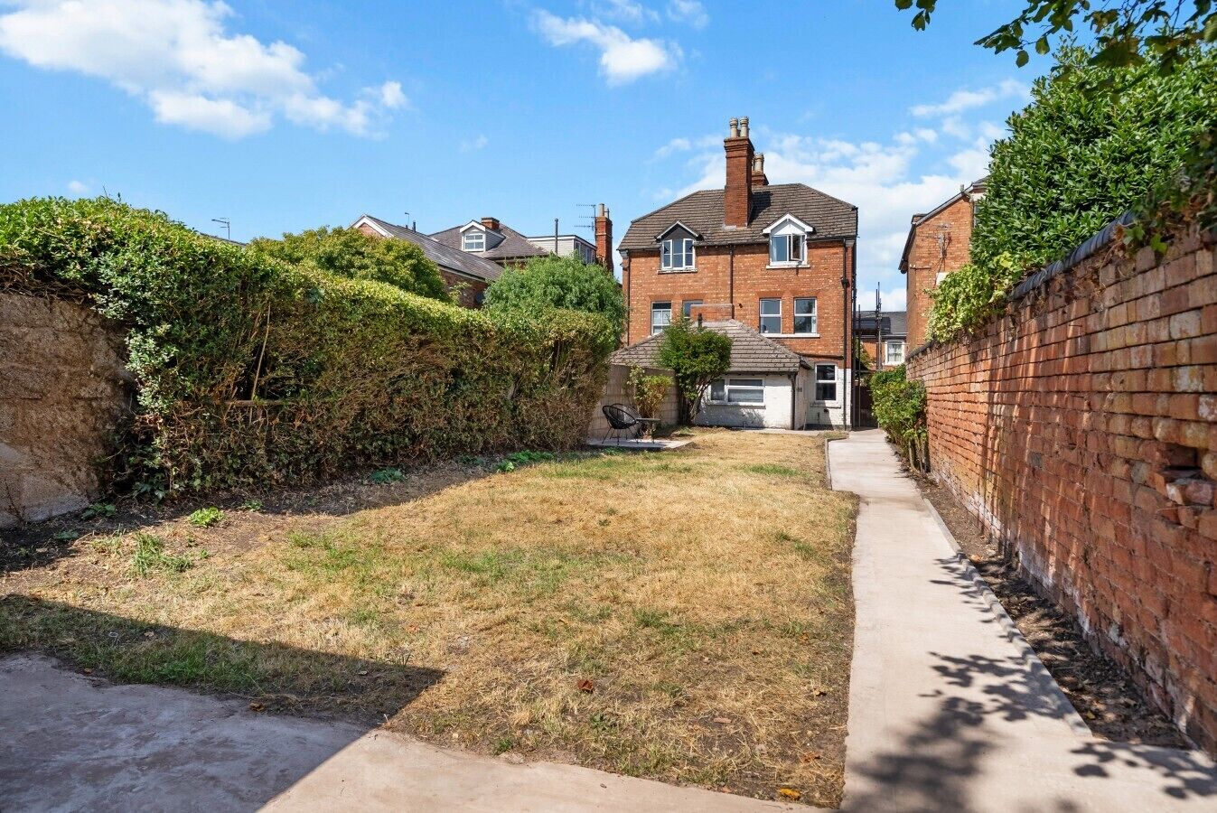 A residential area with a brick house, a paved pathway, and a grassy yard.