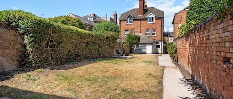 A residential area with a brick house, a paved pathway, and a grassy yard.