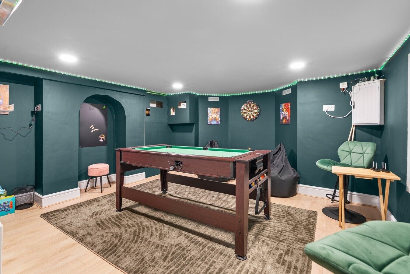 Une pièce avec une table de billard, des cibles de fléchettes et un fauteuil vert.