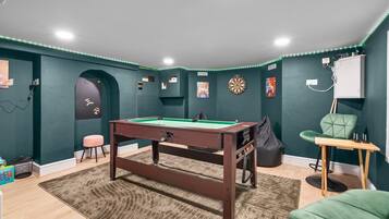 Une pièce avec une table de billard, des cibles de fléchettes et un fauteuil vert.
