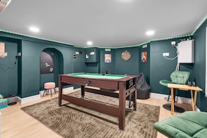 Een kamer met een pooltafel, dartborden en een groene stoel.