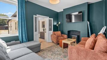 Un salon aux murs de couleur turquoise, avec une cheminée, un téléviseur fixé au mur et un canapé.