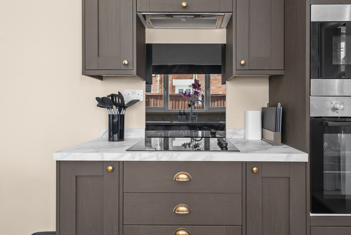 Une cuisine moderne avec des meubles de couleur sombre, un four en acier inoxydable et un plan de travail en marbre.