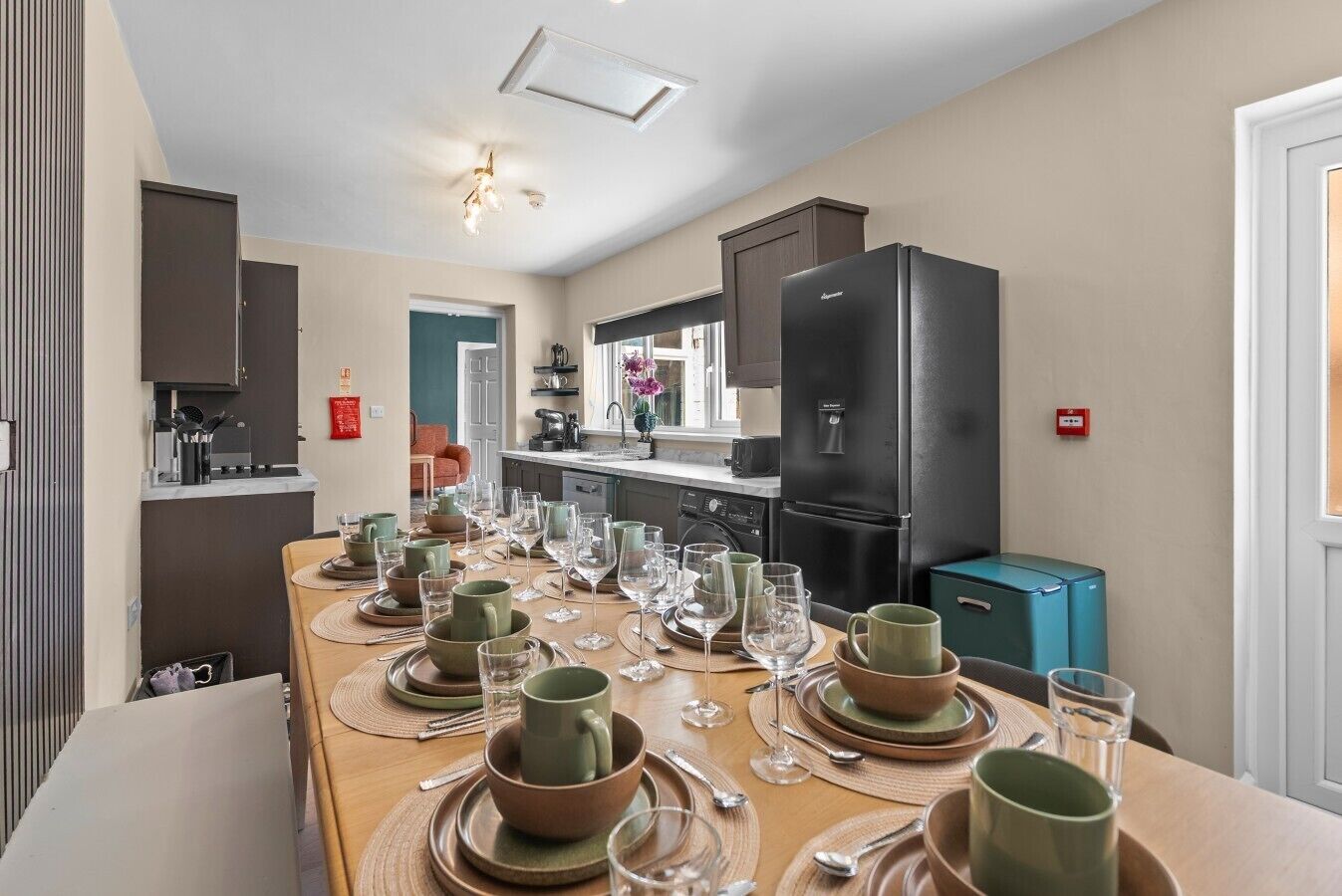 Un coin repas avec une longue table dressée pour le repas, des appareils de cuisine et un réfrigérateur.