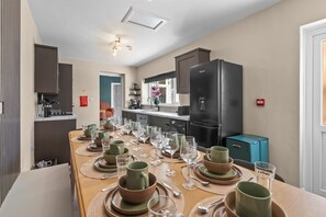 A dining area with a long table set for a meal, kitchen appliances, and a refrigerator. - Luxury Home, Sleeps 12, Pool Table, Free Parking (Worcestershire)