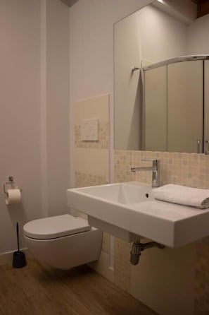 A bathroom with a white toilet, a sink with a towel, and a mirror above the sink. - KRINO' HOTEL&CAFE' (Augusta)