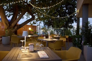 Un espace extérieur aménagé pour les repas, avec des tables et des chaises, des guirlandes lumineuses et des plantes en pot.