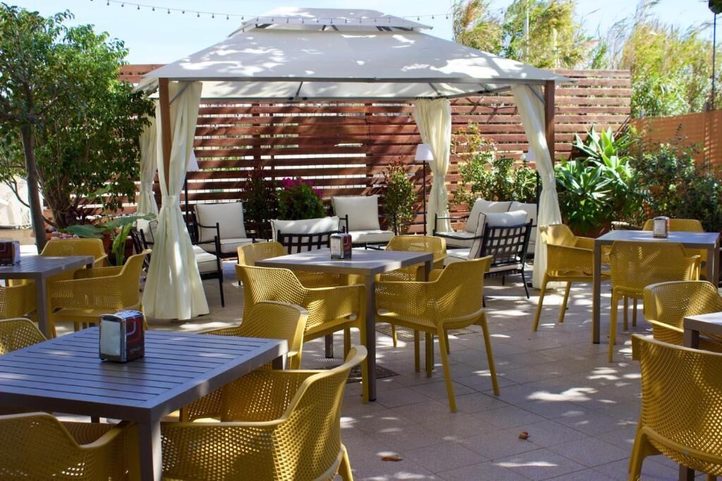 An outdoor patio with yellow chairs and tables, a covered seating area, and a wooden fence in the background.