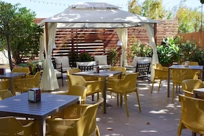 An outdoor patio with yellow chairs and tables, a covered seating area, and a wooden fence in the background. - KRINO' HOTEL&CAFE' (Augusta)