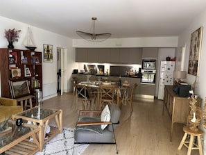 A modern living room with a glass coffee table, a sofa, and a dining area with a table and chairs. - Cozy apartment near the beach - 5 guests (La Teste-de-Buch)