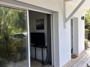 A room with a sliding glass door leading to a balcony, a small table, and a mounted television. - Cozy apartment near the beach - 5 guests (La Teste-de-Buch)
