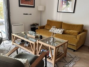 A living room with a glass-top coffee table, a mustard-colored sofa, and a patterned rug. - Cozy apartment near the beach - 5 guests (La Teste-de-Buch)