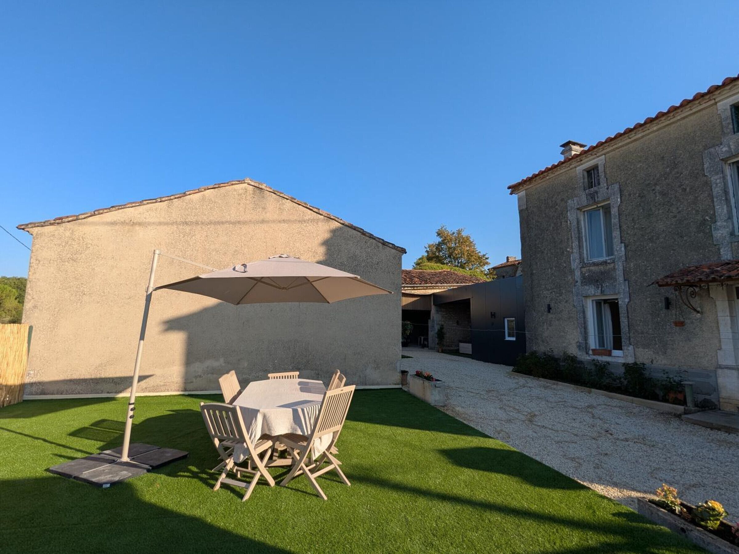 A courtyard with a table and chairs under a large umbrella, surrounded by buildings with stone walls and tiled roofs.
