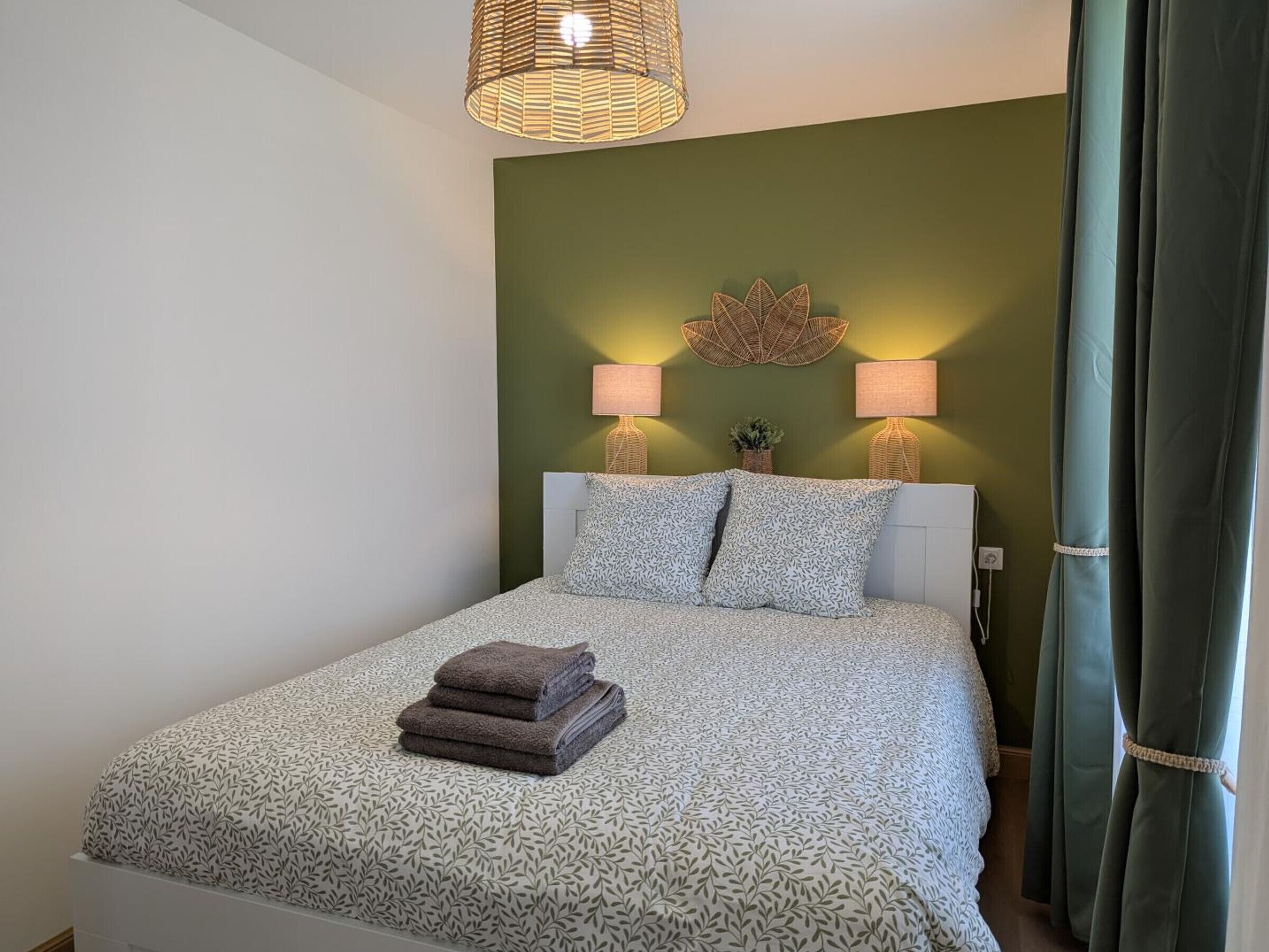 A neatly made bed with a patterned bedspread, two bedside lamps, and a decorative wall piece above the bed.