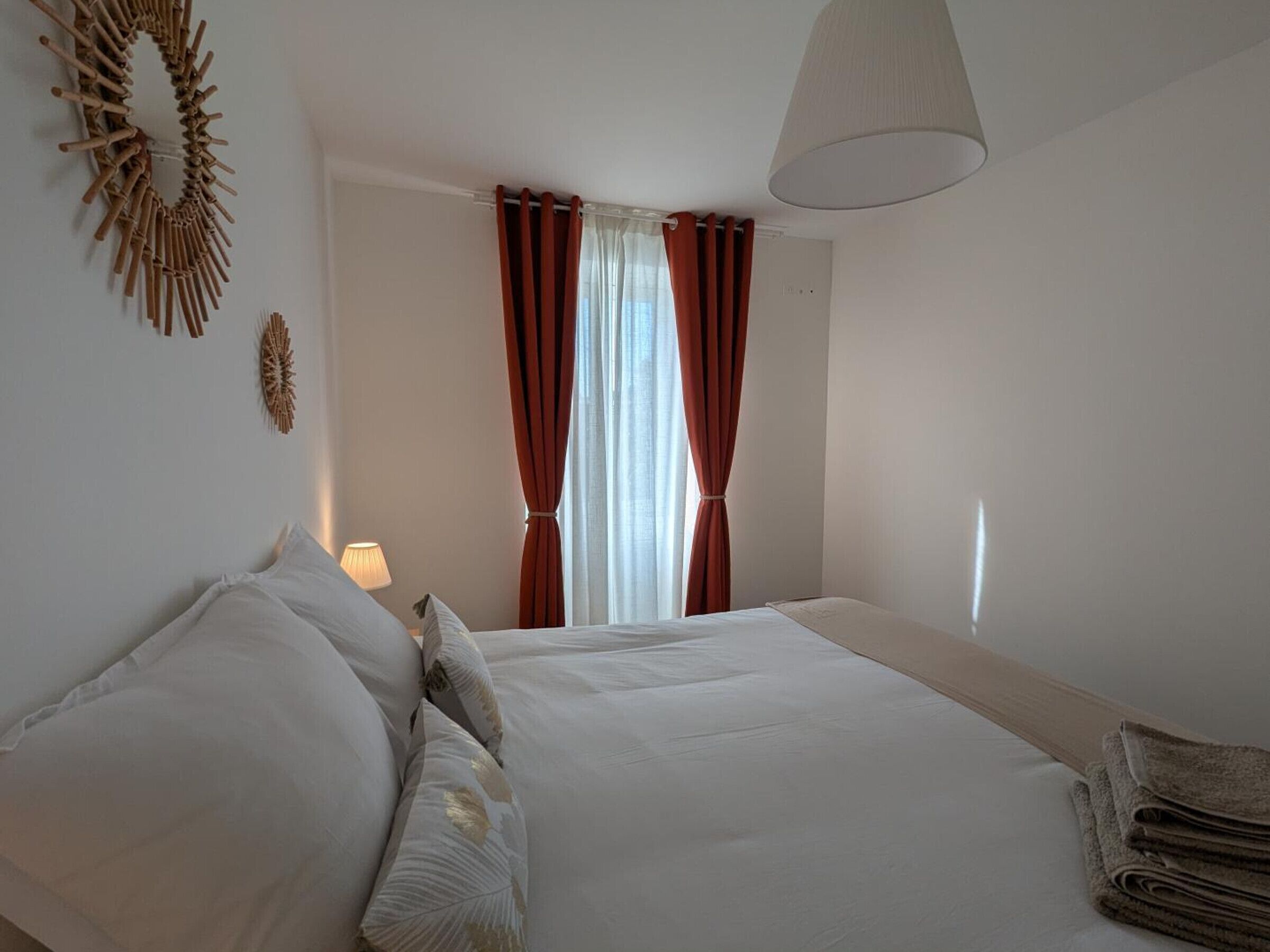 Ein Schlafzimmer mit Bett, Kissen, einer Lampe, Vorhängen und einer Wanddekoration.