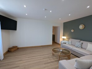 Ein Wohnzimmer mit einer Couch, einem Glastisch und einem an der Wand befestigten Flachbildfernseher.