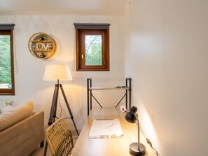 Een kamer met een houten bureau, een lamp, een stoel, een bank en een raam met uitzicht op bomen.