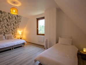 Un dormitorio con dos camas, una ventana, un radiador y una lámpara colgante.