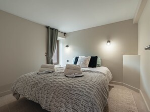 Ein Schlafzimmer mit einem großen Bett, zwei Nachttischen, einem fenster mit Vorhängen und einer Wandleuchte.