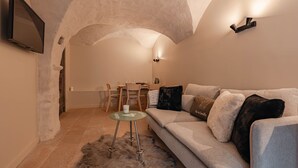A cozy living room with a high, arched ceiling, a grey sofa with multiple cushions, a small glass table with a furry rug, and a dining area with chairs and a table. - Tranquil apartment - 4 guests (Les Belleville)