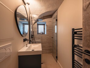 Ein modernes Badezimmer mit einem großen Spiegel, einem Waschbecken, einer Dusche und einem Handtuchhalter.