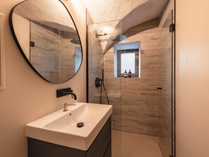 Ein modernes Badezimmer mit einem rechteckigen Waschbecken, einem runden Spiegel und einer Duschkabine aus Glas.