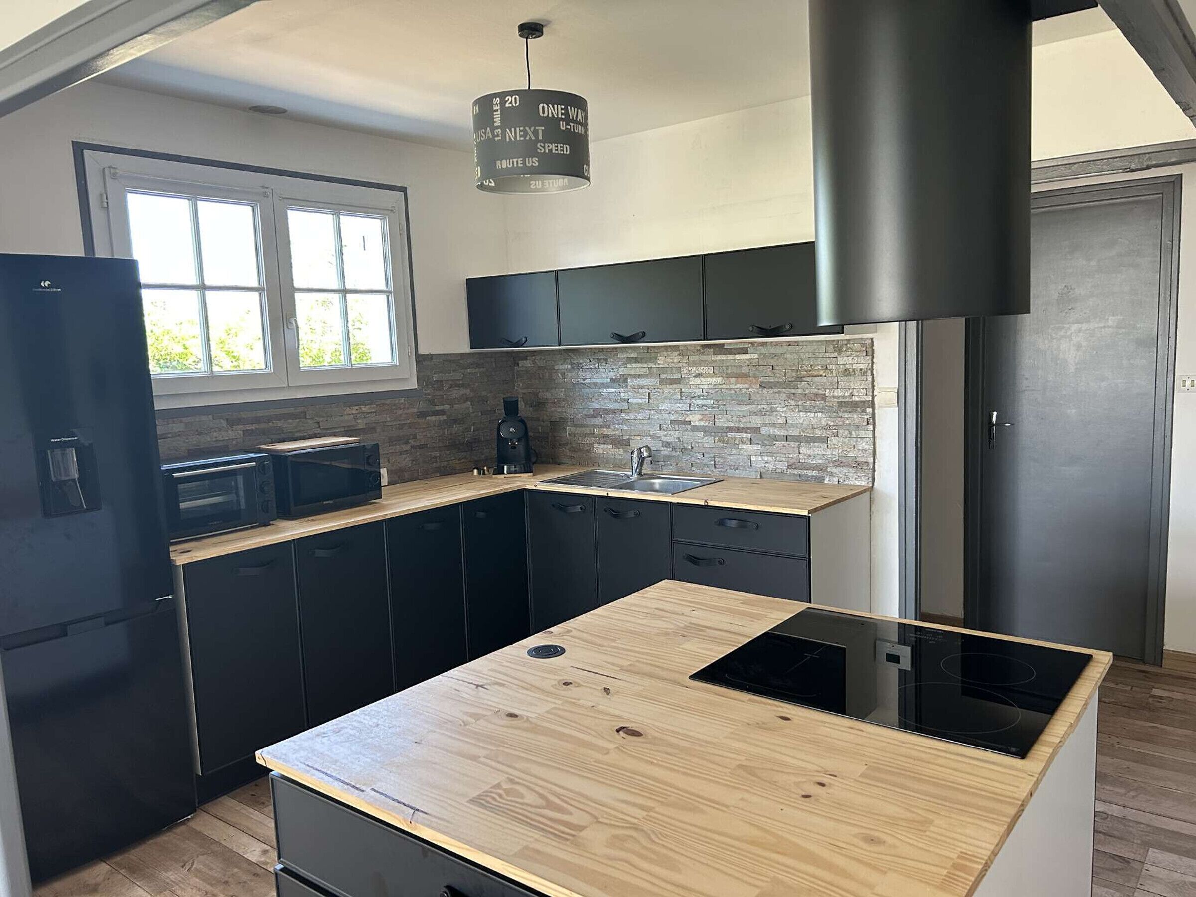 Cocina moderna con encimera de madera, gabinetes negros, pileta de acero inoxidable y campana extractora negra.