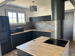 Uma cozinha moderna com bancada de madeira, armários pretos, pia de aço inoxidável e exaustor preto.