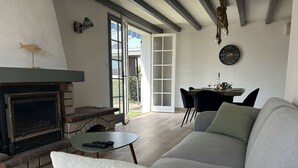 Ein Wohnzimmer mit Kamin, einer Couch, einem Esstisch mit Stühlen und einem großen Fenster.