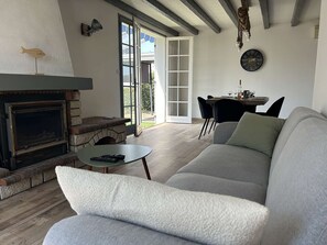 Uma sala de estar com lareira, sofá, mesa de jantar com cadeiras e uma janela grande.