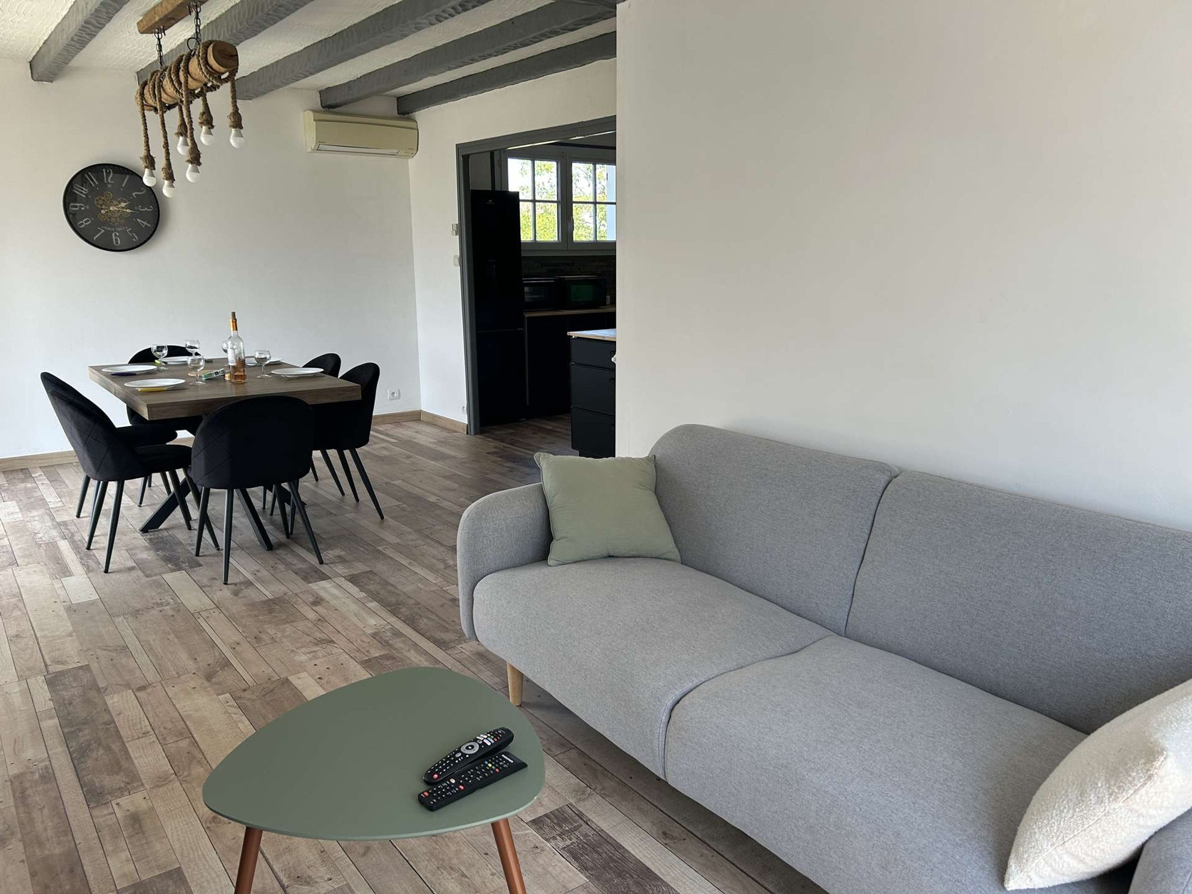 Un soggiorno moderno con un divano grigio, un tavolo da pranzo con sedie e un piccolo tavolino verde con telecomandi.