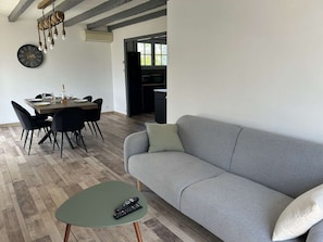A modern living room with a grey sofa, a dining table with chairs, and a small green side table with remotes. - Spacious and tranquil house - 5 guests (Givrand)