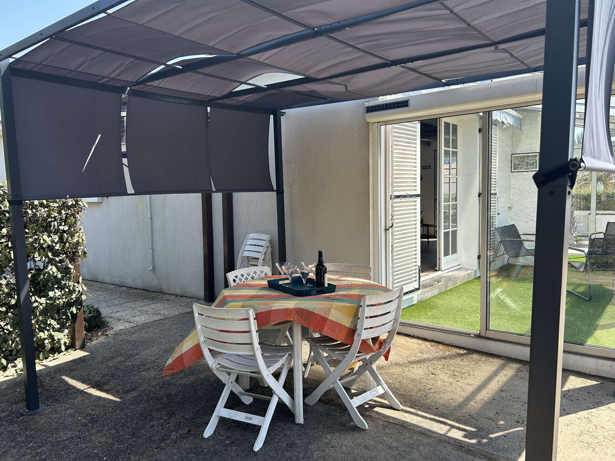 An outdoor patio with a table and chairs, a covered area, and a sliding glass door leading to a garden.