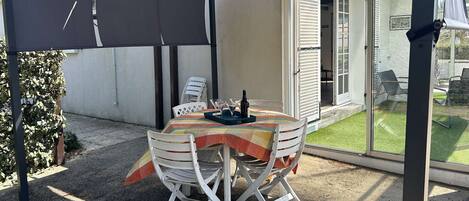 An outdoor patio with a table and chairs, a covered area, and a sliding glass door leading to a garden.