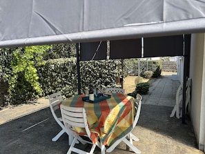 A covered outdoor seating area with a table and chairs, surrounded by greenery. - Spacious and tranquil house - 5 guests (Givrand)