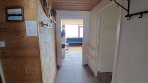 A hallway with wooden walls, a tiled floor, and a door leading to a room with a blue sofa. - Apartment in Vieil Alpe - 6 guests (Huez)