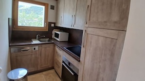 A compact kitchen with wooden cabinets, a microwave, a sink, and a window with a view of greenery. - Apartment in Vieil Alpe - 6 guests (Huez)
