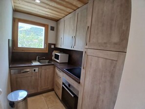 Eine kompakte Küche mit Holzschränken, einer Mikrowelle, einem Spülbecken und einem Fenster mit Blick auf Grünflächen.