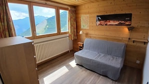 A room with a wooden ceiling, a sofa, a radiator, a window with curtains, and a wall-mounted television. - Apartment in Vieil Alpe - 6 guests (Huez)