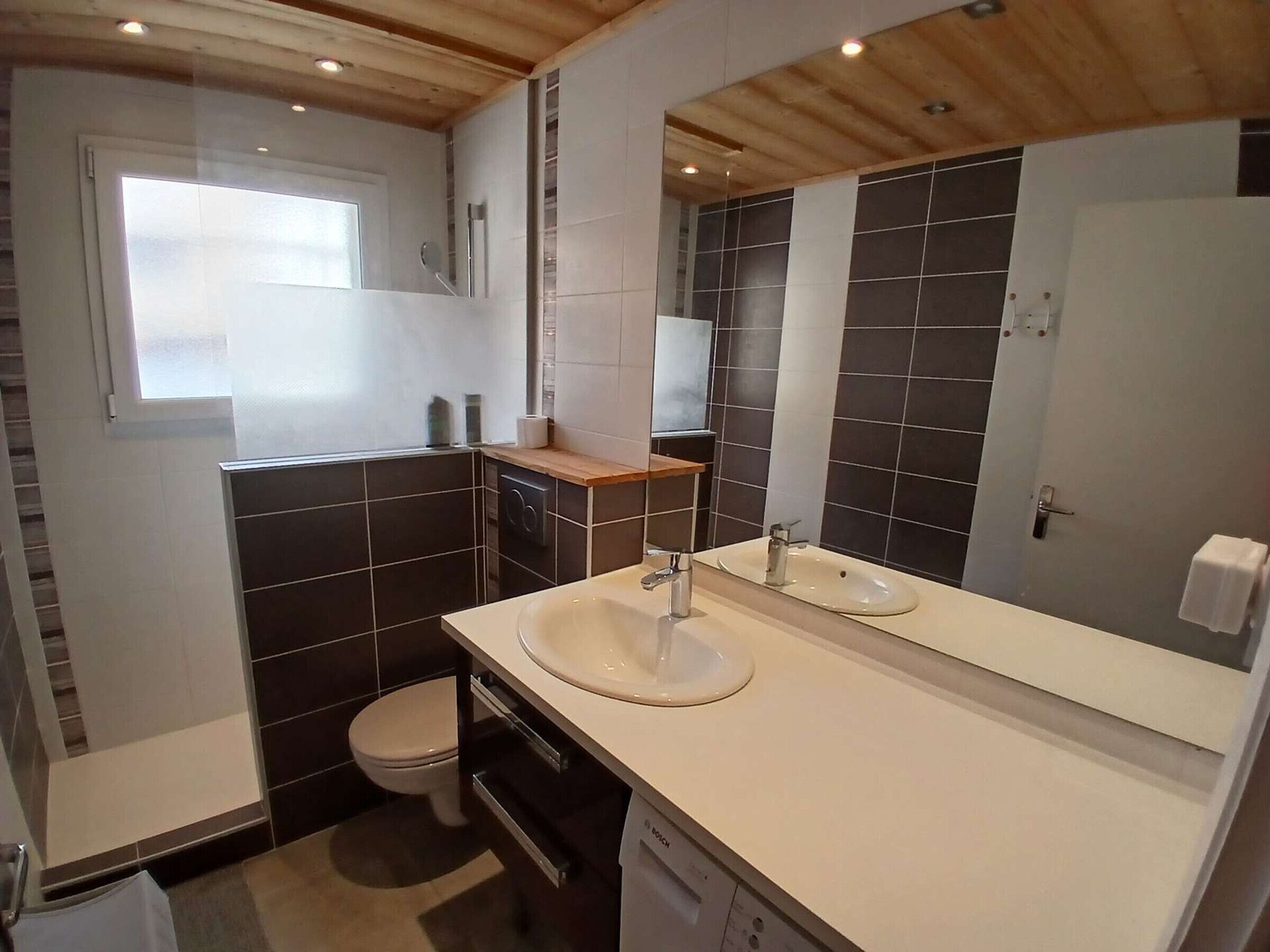 Une salle de bain moderne avec un lavabo blanc, un miroir et des murs recouverts de carreaux foncés.