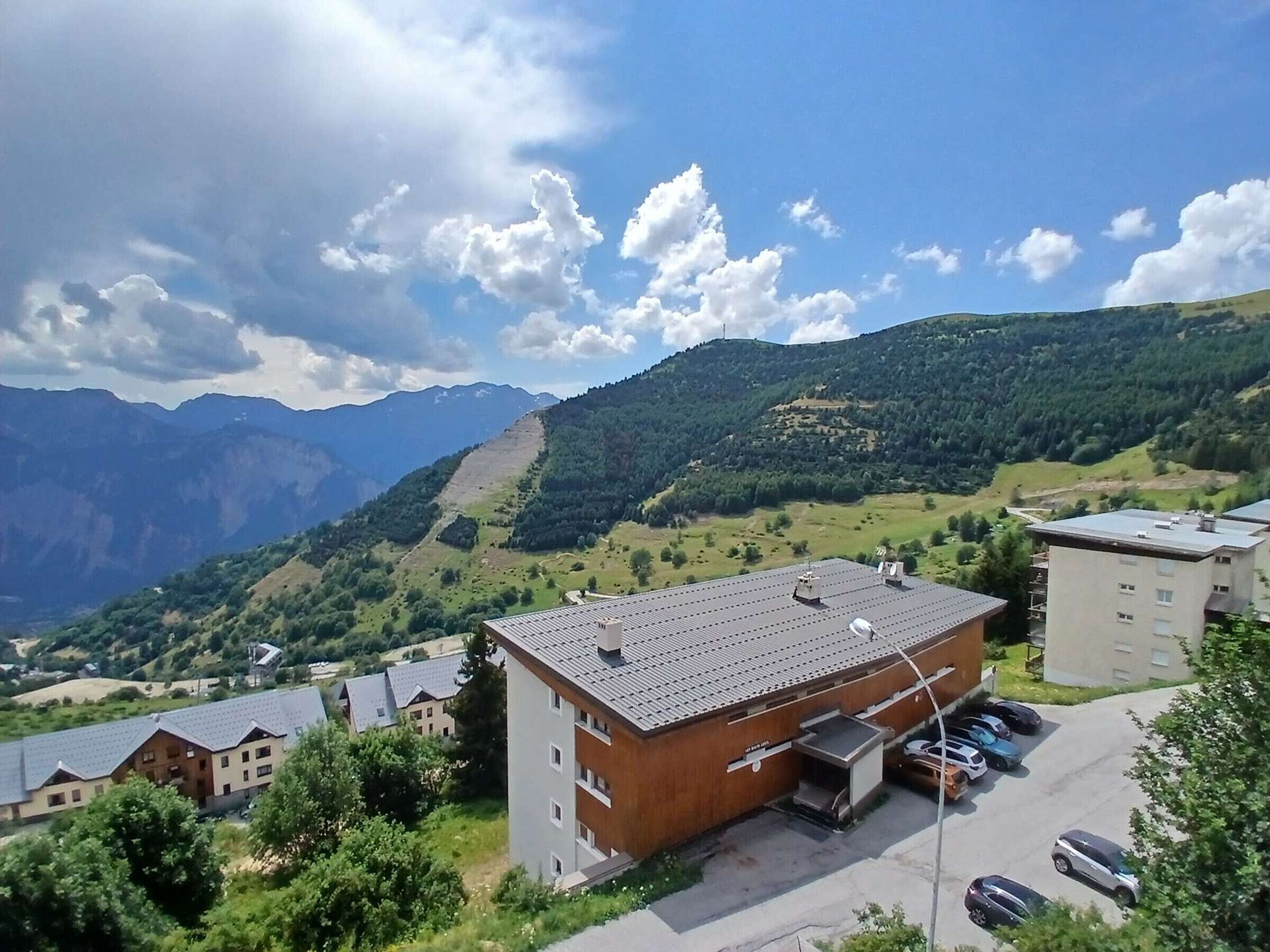 A building with a flat roof, a parking area with cars, and a mountainous landscape in the background.
