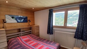A bedroom with a bed, a TV mounted on the wall, a window with curtains, a radiator, and a chair. - Apartment in Vieil Alpe - 6 guests (Huez)