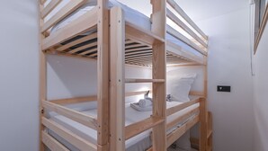 Un llit superposat amb estructura de fusta, matalàs blanc i un coixí.