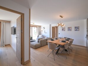 A modern dining area with a wooden table and chairs, a television mounted on the wall, and a ceiling light fixture. - Elegant apartment, panoramic view, mountain - 7 guests (Huez)