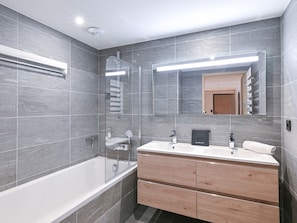 A modern bathroom with a glass-enclosed shower, a white bathtub, and a wooden vanity with a mirror. - Elegant apartment, panoramic view, mountain - 7 guests (Huez)